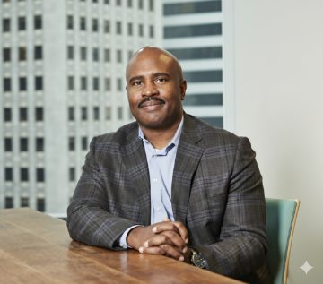 A distinguished-looking man, dressed in business attire, seated at a desk with a subtle office background, ideal for a professional profile or team page.