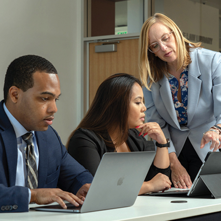 Students working on laptops with faculty instructing the students
