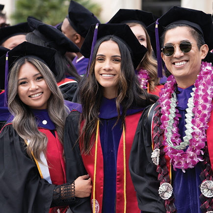 Students in graduation garb smiling for the camera