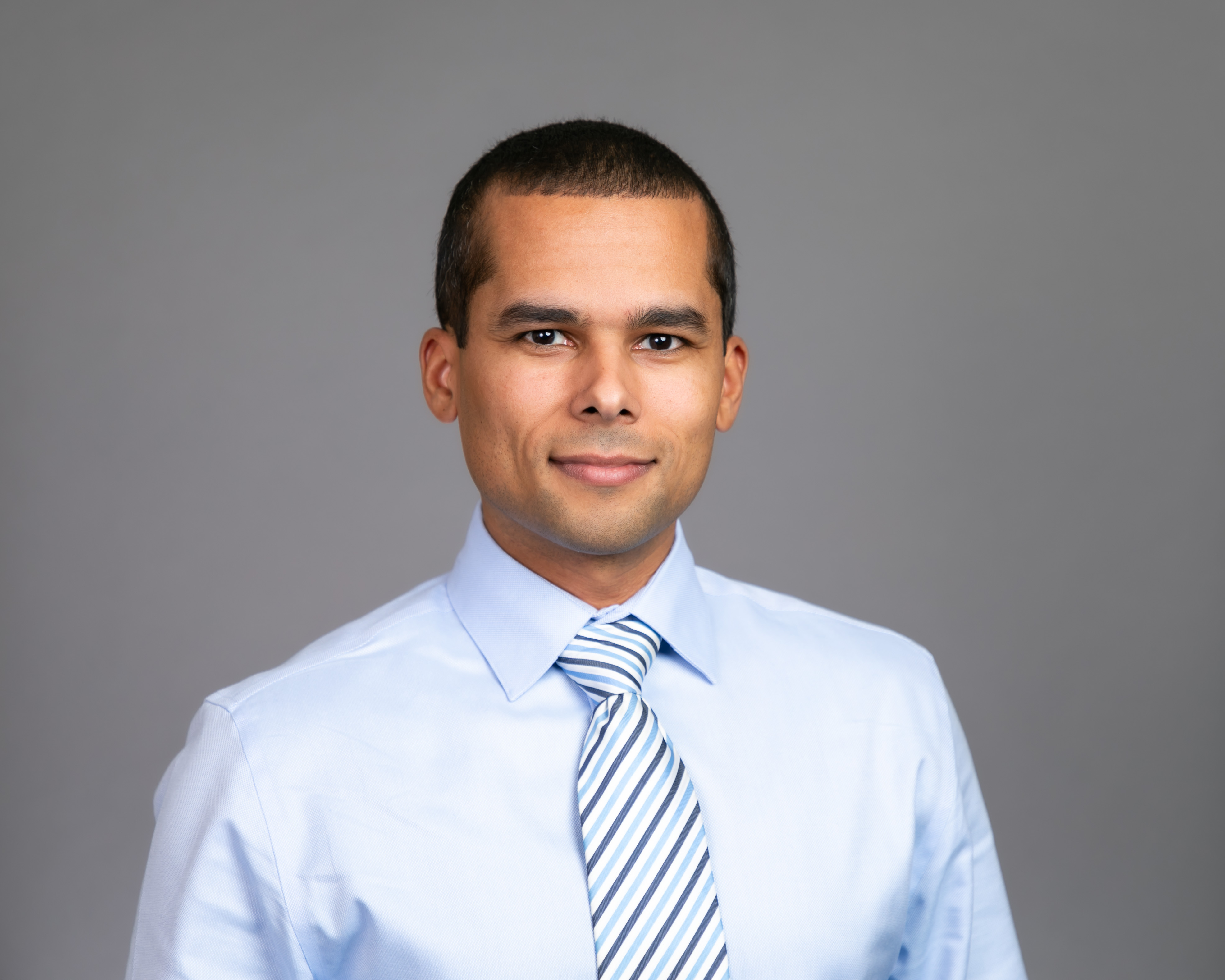 headshot of prof brandon honore a man with brown hair wearing a light blue shirt and blue striped tie