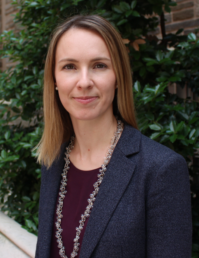 photo of prof erika douglas a white woman with light brown hair wearing a maroon shirt, a blue tweed blazer and a silver necklace the background is a brick building and greenery