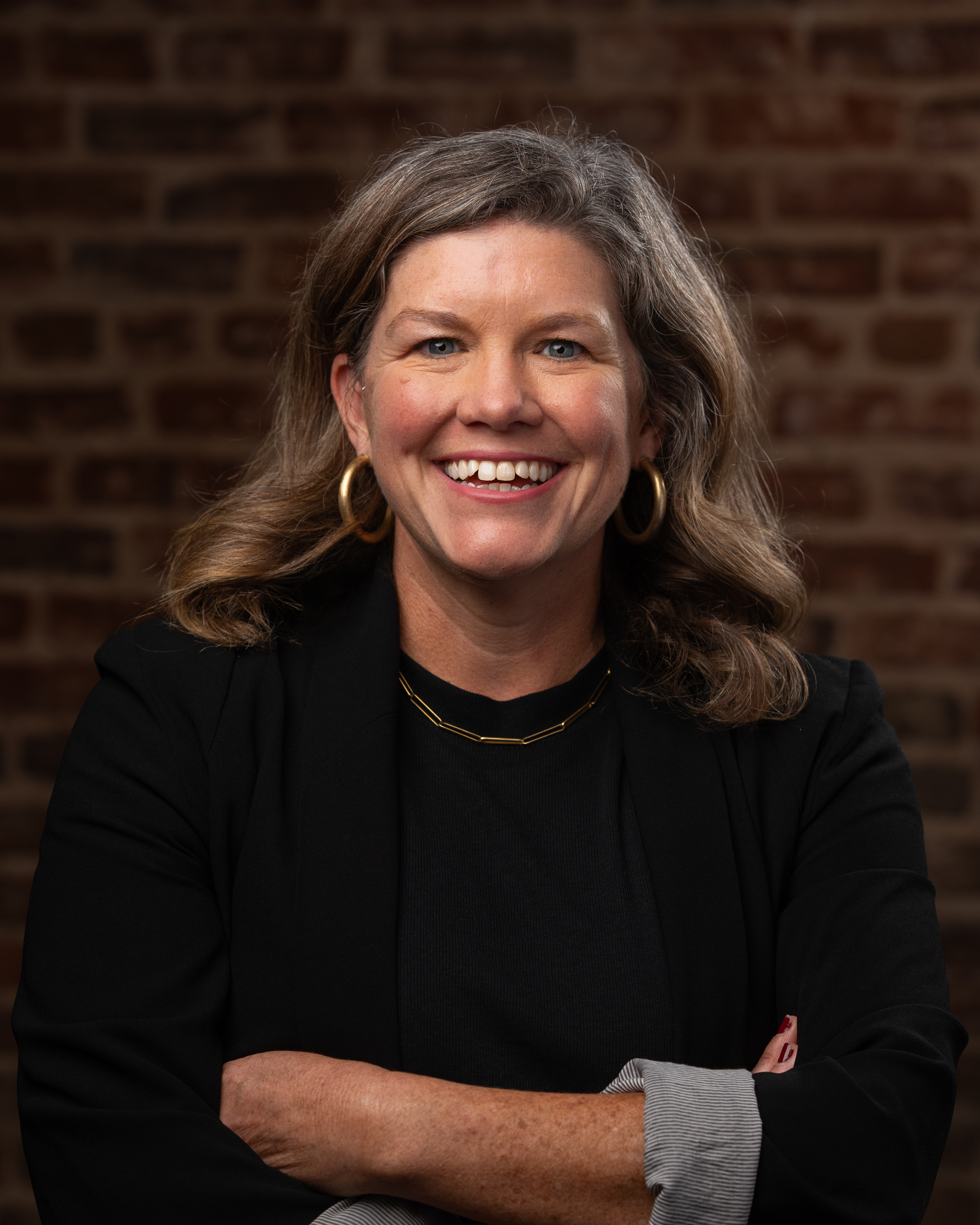 photo of prof megan crane a smiling woman with light brown hair wearing a black shirt and gold necklace and earrings