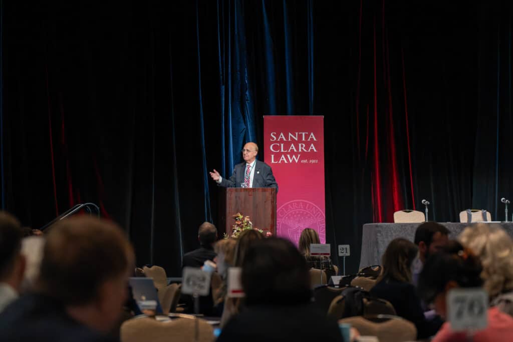 person in a suit talking at an event on stage 