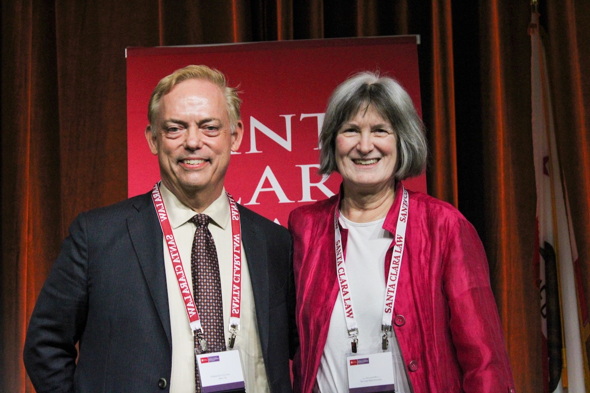 a man and woman smiling in front of a Santa Clara Law banner