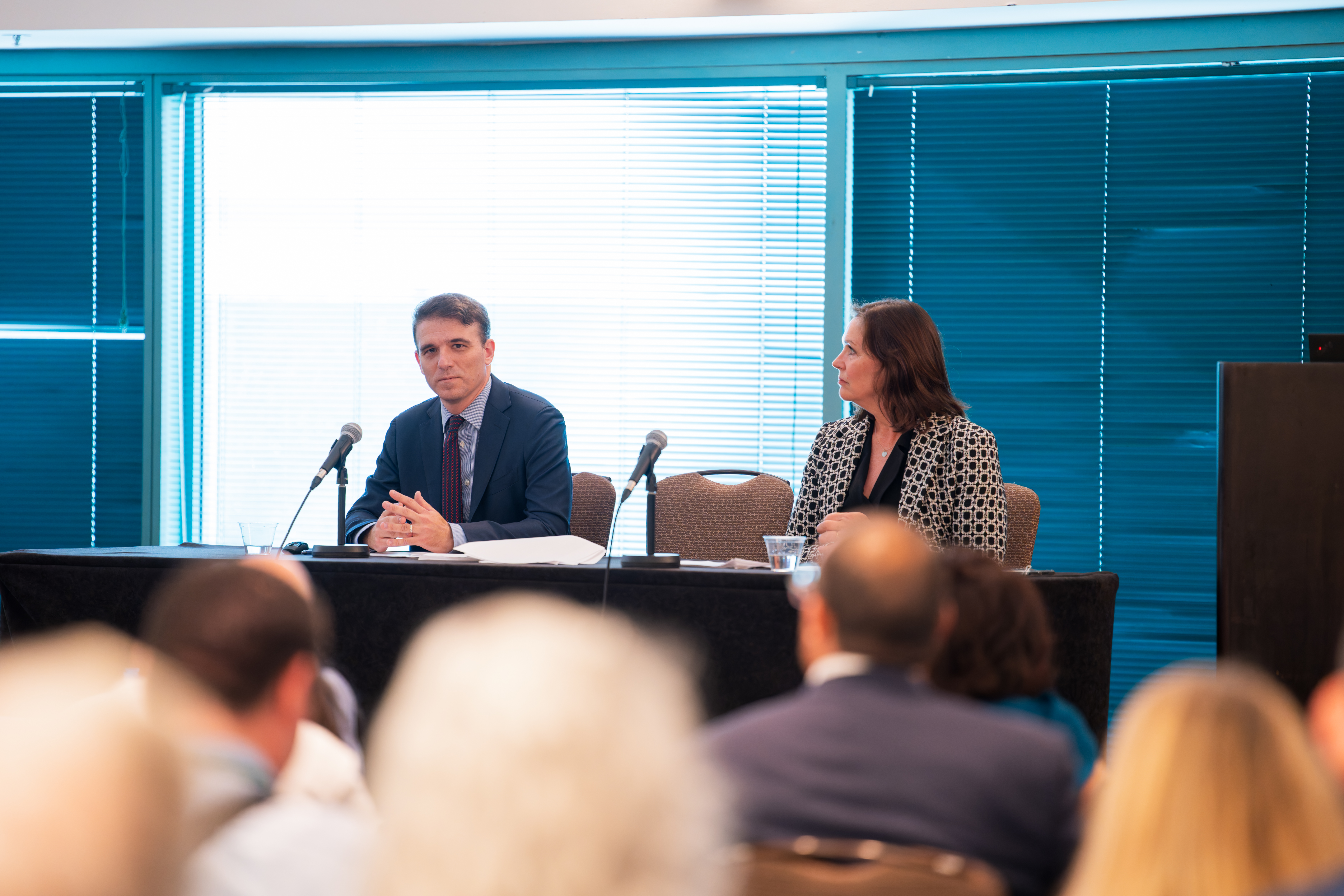 A man and women on stage at an event speaking to a crowd of people.