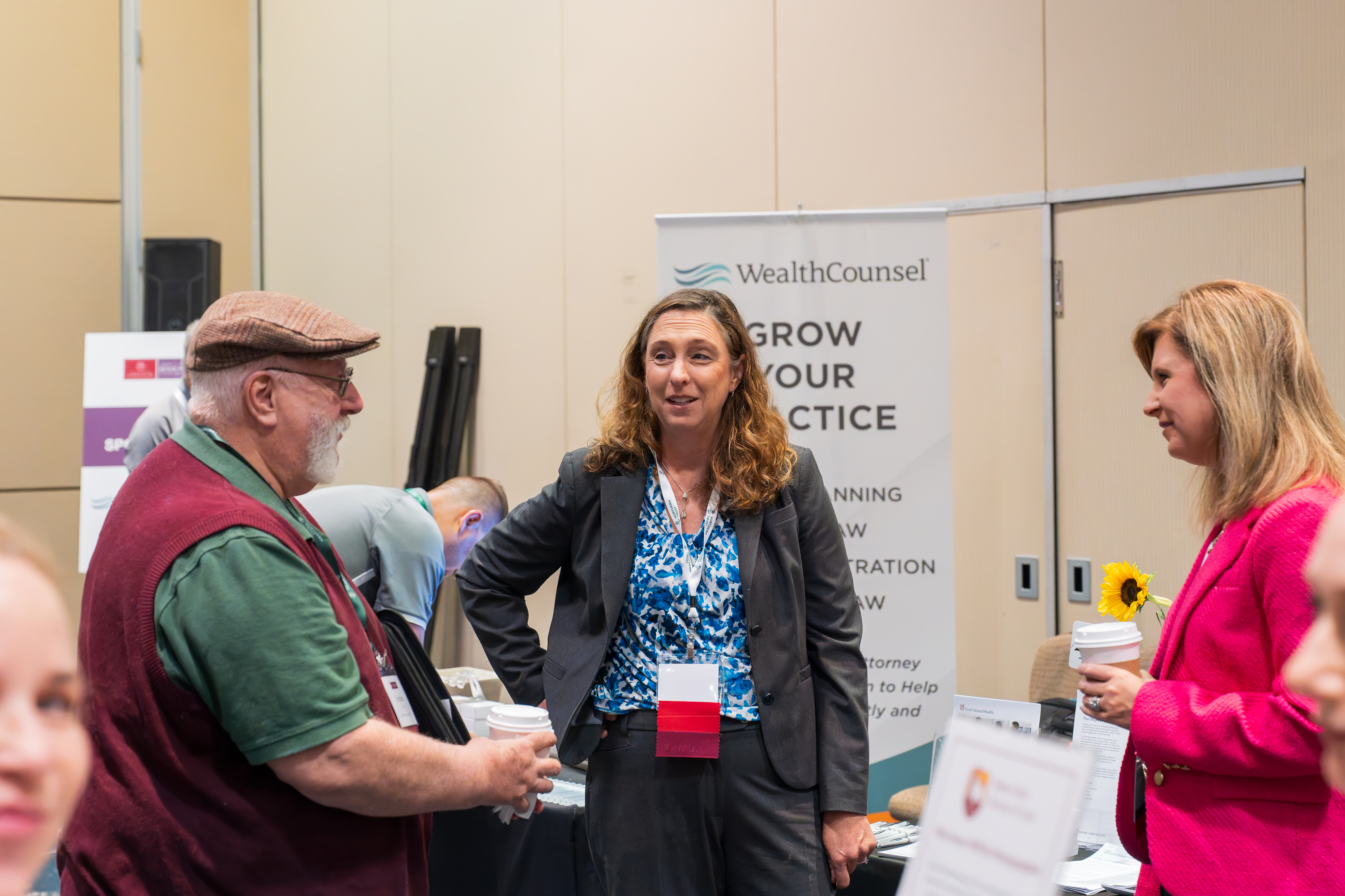 Three people standing and talking at a booth at an event.