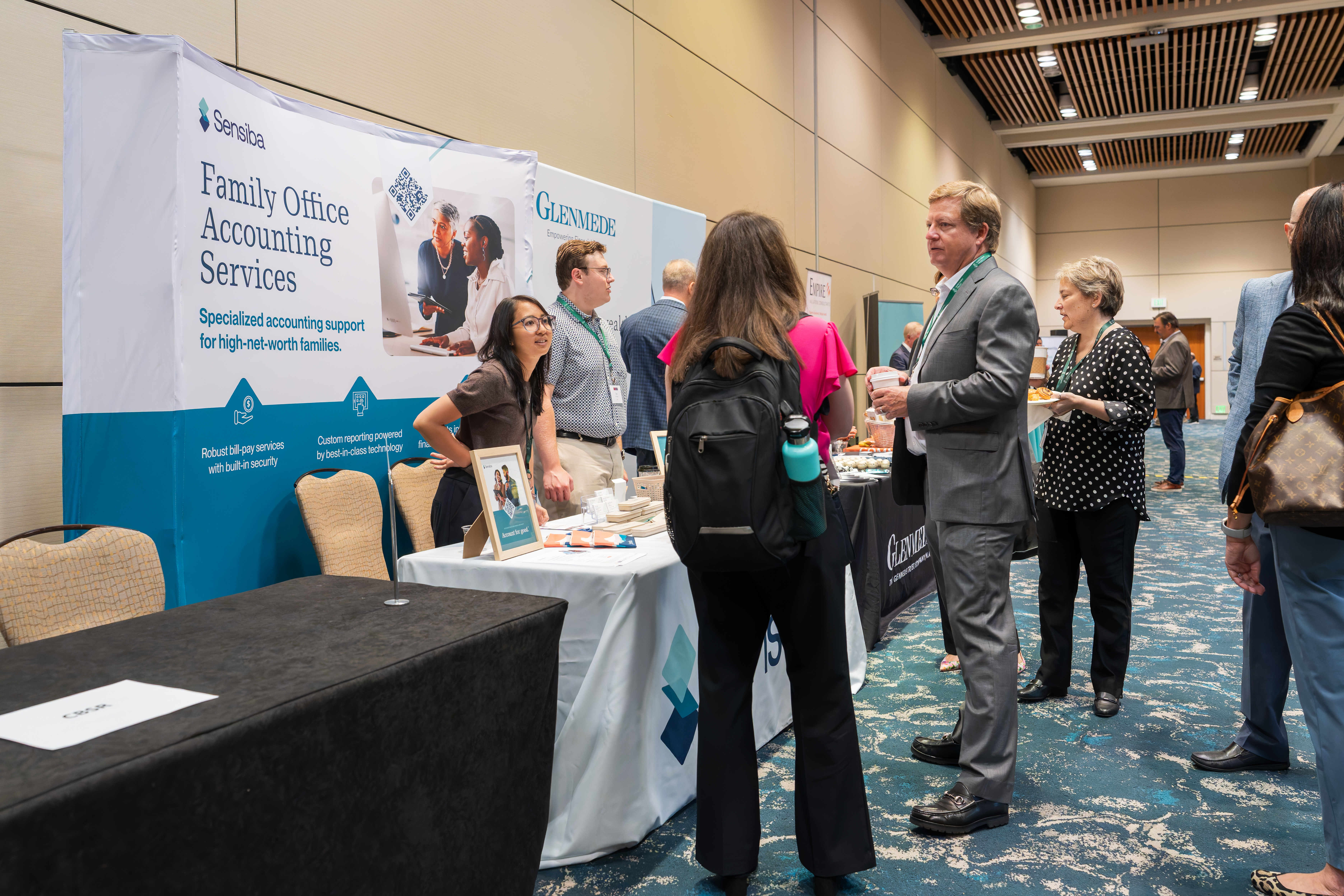 A group of people standing at a hotel convention for an event with bunch of booths.