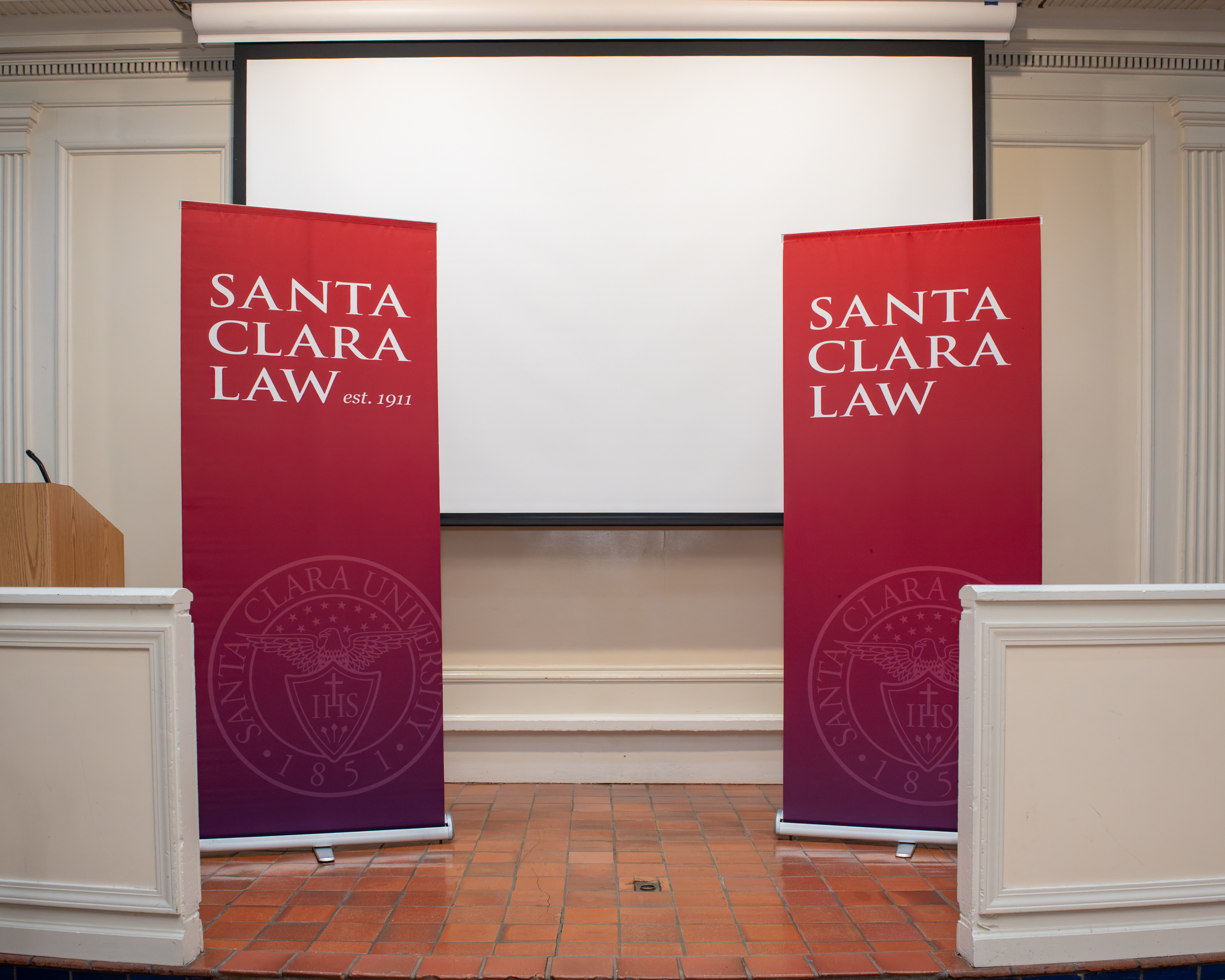 two banners that have the worlds Santa Clara Law in front of a projector screen in a event room