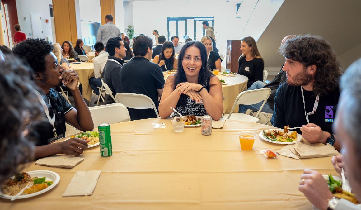 Three students sitting and dining around circular table and smiling
