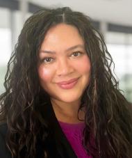 A portrait of a smiling woman with long, dark, wavy hair.